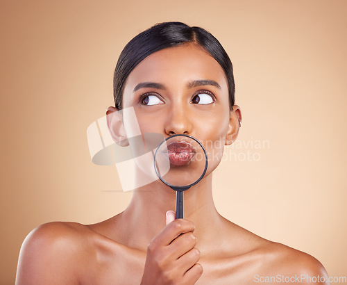 Image of Mouth, lips or woman with magnifying glass in studio on beige background searching for facial beauty. Face, headshot or young Indian girl looking for luxury self care cosmetics, lipstick or makeup