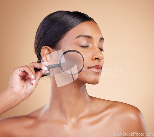 Image of Skincare, model face or woman with magnifying glass in studio on beige background searching for beauty. Facial, eyes closed or young Indian girl looking for luxury self care cosmetics or makeup