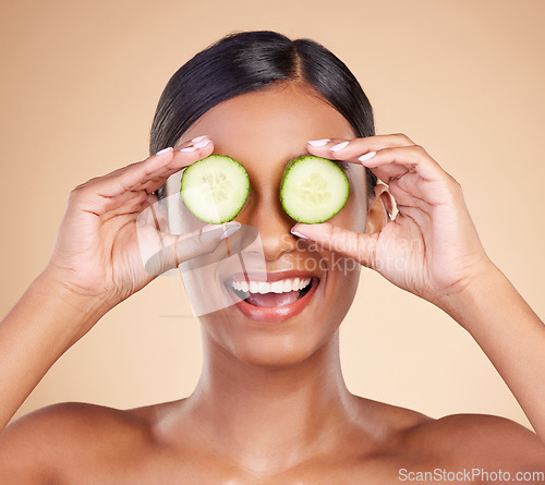 Image of Woman, face and cucumber for natural skincare, beauty and nutrition cosmetics against a studio background. Happy female holding vegetables with smile for healthy organic facial, diet or spa treatment