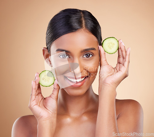 Image of Portrait, beauty and cucumber with a woman in studio on a beige background to promote natural skincare. Face, fruit and organic with an attractive young female posing for cosmetics or luxury wellness