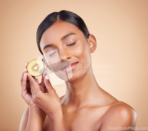 Image of Woman, kiwi and natural skincare, beauty and nutrition cosmetics against a studio background. Calm and happy female model holding fruit with smile for healthy organic facial, diet or spa treatment