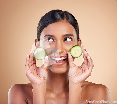 Image of Woman, thinking and cucumber for natural skincare, beauty and nutrition cosmetics against a studio background. Happy female holding vegetables in thought for healthy organic diet or facial treatment