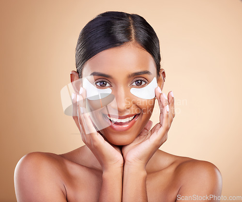 Image of Beauty, eye patch and portrait of a woman in studio for skincare, dermatology and cosmetics. Happy Indian female model with smile and collagen mask for self care moisture facial on brown background