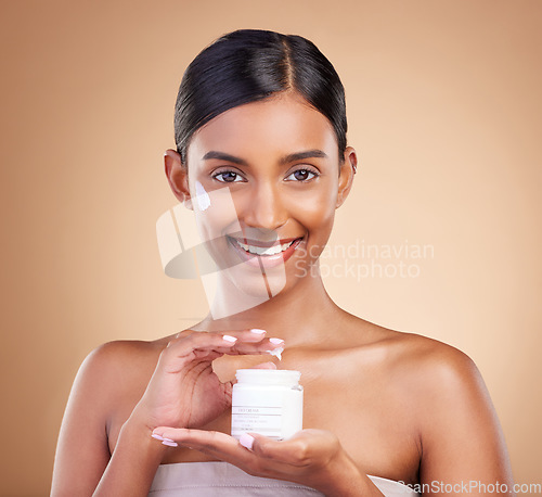 Image of Portrait, product and cream with a model woman in studio on a beige background for beauty or skincare. Face, advertising and lotion with an attractive young female holding a cosmetics container