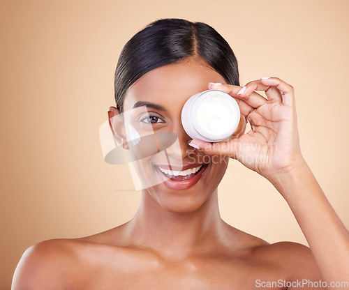 Image of Beauty, face cream and portrait of a woman in studio for skincare, dermatology and cosmetics. Happy Indian female model with smile and lotion on hand for self care moisture facial on brown background