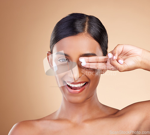 Image of Beauty, face cream and portrait of a woman in studio for skincare, dermatology and cosmetics. Happy Indian female model with smile and lotion on hand for self care moisture facial on brown background