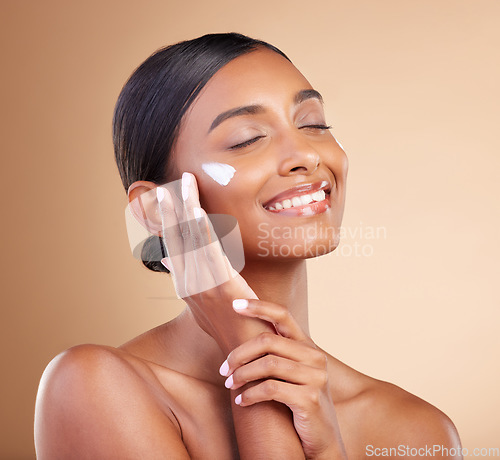 Image of Woman, face and smile with skincare moisturizer cream for beauty cosmetics or self care against studio background. Happy female model applying lotion, creme or product in satisfaction for spa facial