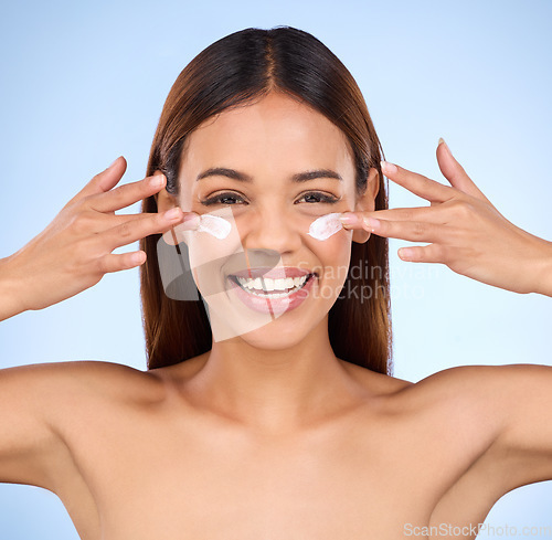 Image of Skincare, beauty and portrait of happy woman with eye cream, anti aging or skin care on blue background. Cosmetics, facial lotion and face of hispanic model with smile and collagen product in studio.