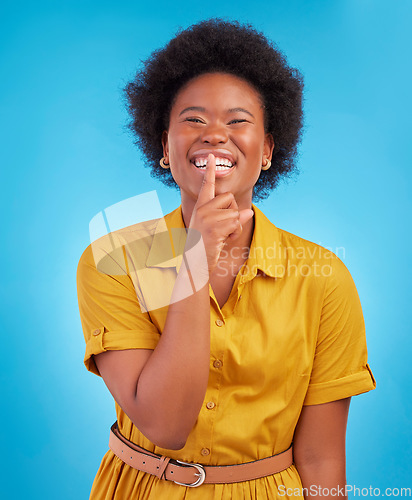 Image of Portrait, smile and secret with a black woman in studio on a blue background standing finger on lips. Gossip, whisper and mystery withan attractive young female making a hand gesture emoji of privacy