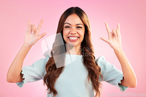 Image of Portrait of woman, smile and rock hand gesture in studio, happy expression on face on pink background. Culture, hispanic model and hands in devil horn sign or emoji, punk attitude and happy symbol.