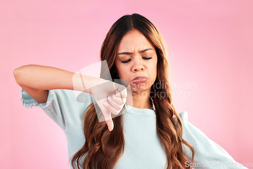 Image of Unhappy, thumb down and sad woman in a studio with an upset, moody or disappointed face. Loser, rejection and young female model posing with a disagreement hand gesture isolated by a pink background.