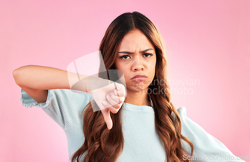 Image of Upset, thumbs down and portrait of a female in a studio with a sad, moody or disappointed face. Loser, unhappy and young woman model posing with a angry hand gesture isolated by a pink background.