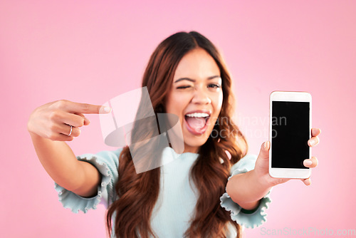 Image of Phone screen, wink and woman pointing to mockup in studio isolated on pink background. Cellphone, face portrait or happy female with mobile smartphone for advertising, marketing or product placement.