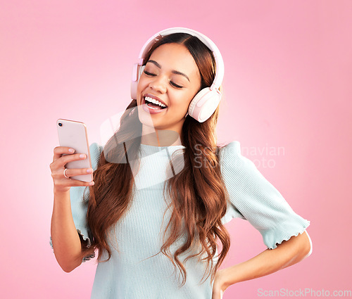 Image of Phone, music headphones and woman singing in studio isolated on a pink background. Cellphone, radio singer and happy female with mobile streaming, laughing and listening to audio, sound or podcast.