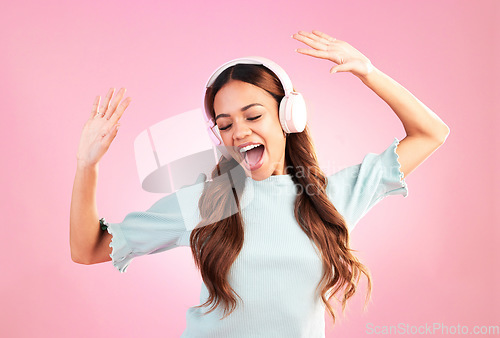 Image of Music headphones, dancing and woman singing in studio isolated on a pink background. Singer, radio dance and happy mixed race female streaming, enjoying and listening to audio, sound track or podcast