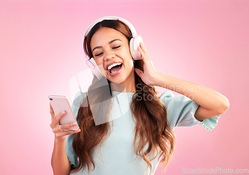 Image of Music headphones, phone and woman singing in studio isolated on a pink background. Cellphone, radio singer and happy female with mobile streaming, enjoying and listening to audio, sound or podcast.