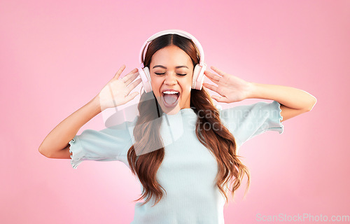 Image of Music headphones, singing and woman dance in studio isolated on a pink background. Singer, dancing and happy mixed race female streaming, enjoying and listening to audio, sound track or radio podcast