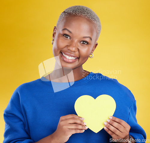 Image of Paper heart, portrait and happy black woman in studio, background and color backdrop. Smile, female model and yellow shape for love, wellness and caring support of peace, romance and sign of kindness