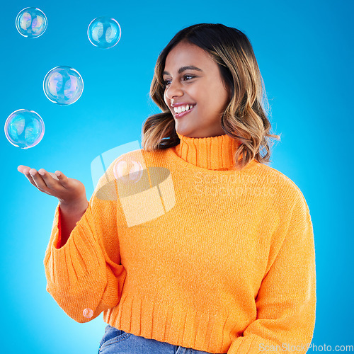 Image of Happy, holding and bubble with indian woman in studio for soap, positive and satisfaction. Magic, creative and smile with female isolated on blue background for bright, cute and entertainment