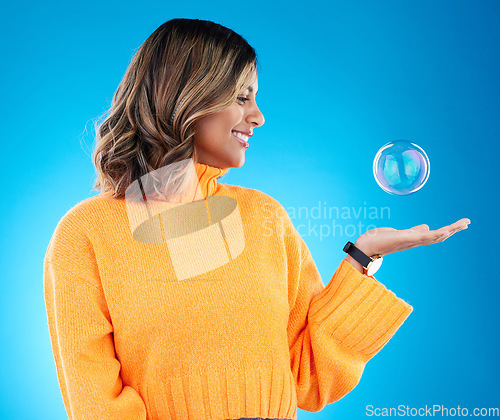 Image of Happy, smile and bubble with indian woman in studio for soap, positive and satisfaction. Magic, creative and holding with female isolated on blue background for bright, cute and entertainment