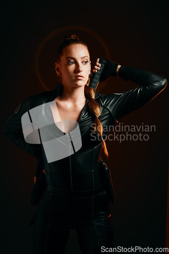 Image of Woman, warrior and costume of vigilante in cosplay ready for battle, war or game against a dark studio background. Female in black leather uniform with sword and guns for halloween or hunger games