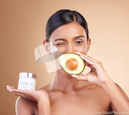 Image of Beauty, avocado and face cream woman portrait in studio for cosmetics, skin glow and natural product. Indian female model wink on beige background for skincare, facial self care and organic container