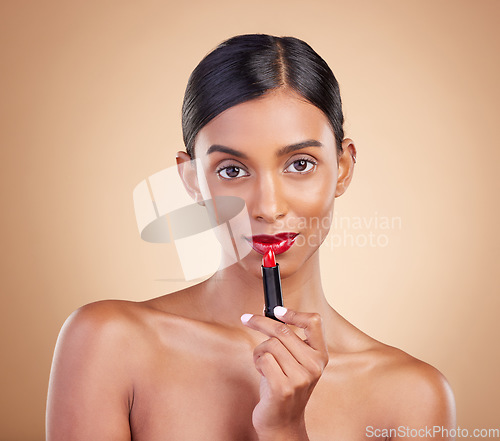 Image of Indian woman, lipstick product and studio portrait for beauty, wellness or skincare by brown background. Asian model, girl and red makeup on lips with natural glow, self care or cosmetology for youth