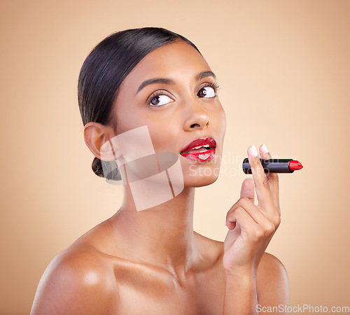 Image of Beauty, red lipstick and makeup on a woman in studio for cosmetics, skin glow and shine product. Indian female model thinking on beige background for skincare, facial self care and lips with color
