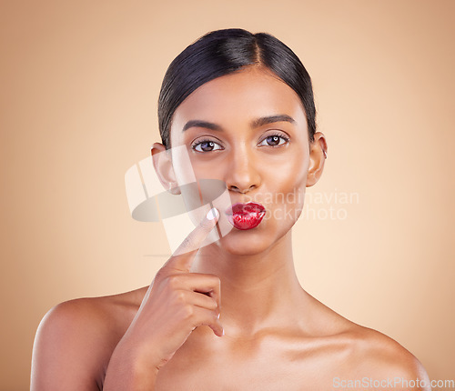 Image of Beauty, red lipstick and makeup portrait of a woman in studio for cosmetics, skin glow and shine. Indian female model with finger on face or kiss on beige background for self care and lips with color