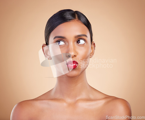 Image of Red lipstick, beauty and makeup on a woman in studio for cosmetics, skin glow and shine product. Indian female model thinking and kiss on beige background for skincare, self care and lips with color