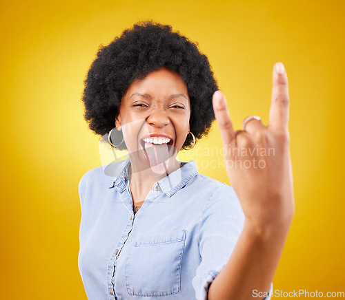Image of Rock hand, metal and black woman portrait in studio with tongue out for punk music. Happiness, freedom and cool young female with isolated yellow background feeling edgy with rocker hands sign