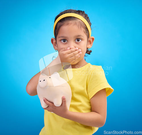 Image of Piggy bank, shocked or surprised child in portrait isolated on blue background savings mistake or investment risk. Wow face of girl kid and saving jar or container for finance or money fear in studio