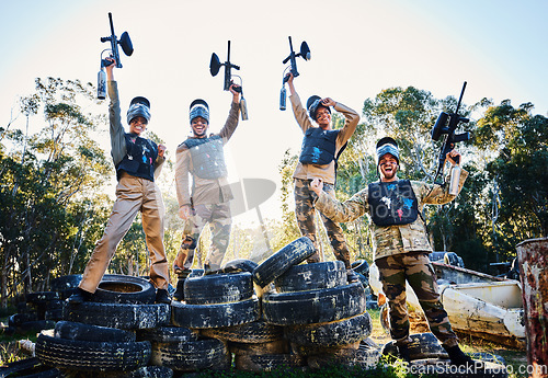 Image of Team, paintball and portrait in celebration for winning, victory or achievement standing on tires together in nature. Group of people enjoying win, success or teamwork with guns in the air for sports