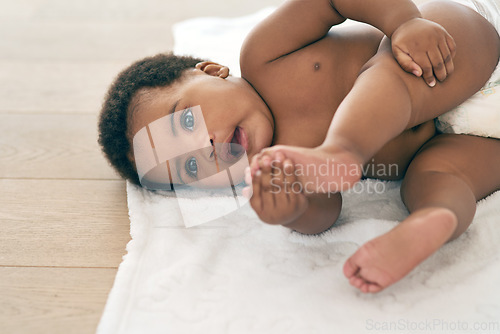 Image of Baby, infant and black child lying down newborn relax in a home, nursery or house floor with a diaper playing with feet. Cute, adorable and innocent little kid with happiness in development