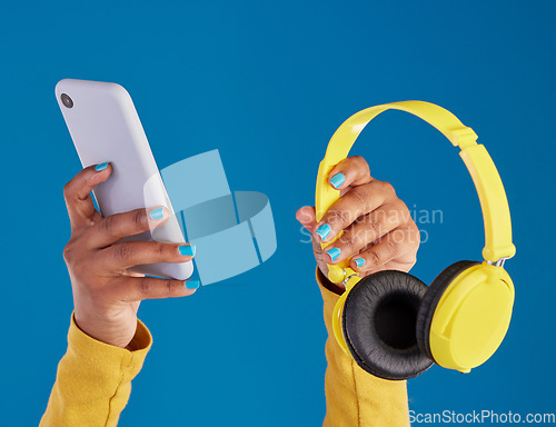 Image of Closeup, hands and smartphone with headphones, streaming music and audio against blue studio background. Zoom, hand and technology with cellphone, headset or radio with sounds, internet or connection