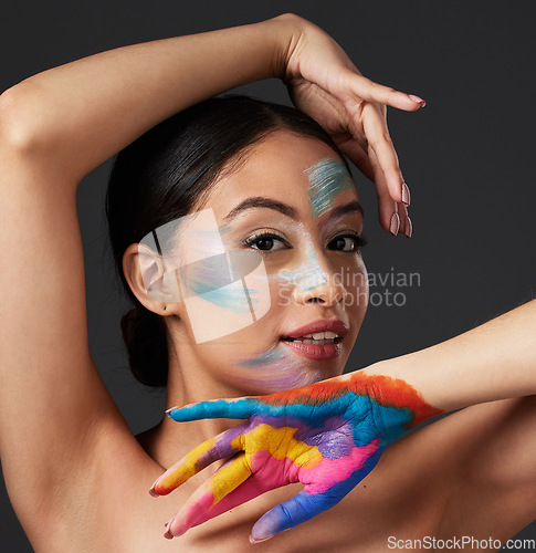 Image of Woman, portrait and beauty with rainbow paint art on hand and face in studio with a smile. Creative skin and makeup on female aesthetic model on gray background for lgbtq color inspiration on hands