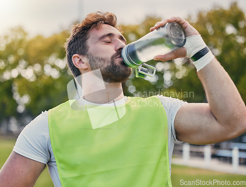 Image of Drinking water, fitness and hydration with a sports man outdoor for a competitive game or event. Exercise, training and health with a male athlete taking a drink from a bottle during a break or rest