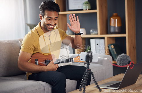 Image of Podcast, guitar and laptop with a man online to wave and coach during live streaming lesson. Asian male person happy on home sofa with a ukulele as content creator teaching music on education blog