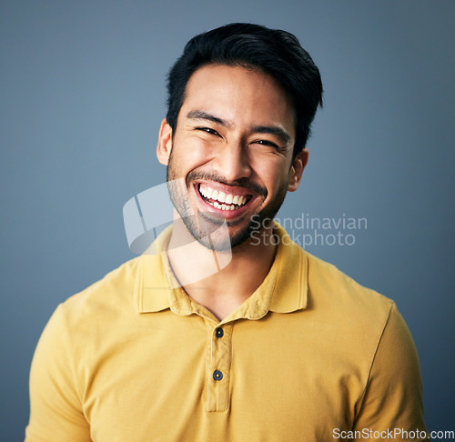 Image of Portrait, happy and carefree with a man in studio on a blue background feeling confident or positive. Face, smile and cheerful with a handsome young male posing on a color wall looking relaxed