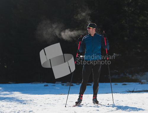 Image of Portrait handsome male athlete with cross country skis, taking fresh breath and having break after hard workout training in a snowy forest. Healthy winter lifestyle concept