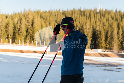 Image of Handsome male athlete with cross country skis preparing equipment for training in a snowy forest. Checking smartwatch. Healthy winter lifestyle.