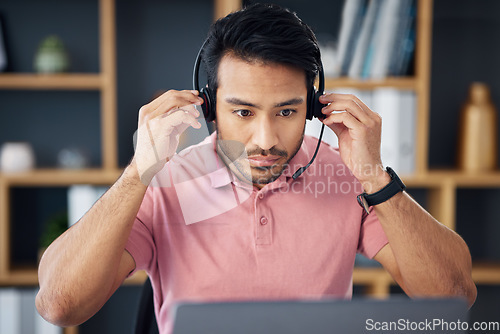 Image of Serious asian man, call center and headset on laptop for consulting, customer service or support at office desk. Focused male consultant putting on headphones by computer for telemarketing or advice