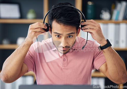 Image of Asian man, call center and headset on laptop ready for consulting, customer service or support at office desk. Serious male consultant putting on headphones by computer for telemarketing or advice