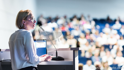 Image of Female speaker giving a talk on corporate business conference. Unrecognizable people in audience at conference hall. Business and Entrepreneurship event.