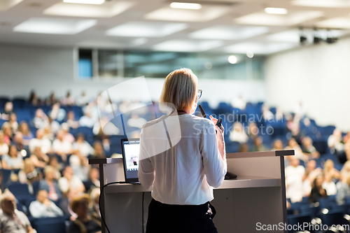 Image of Female speaker giving a talk on corporate business conference. Unrecognizable people in audience at conference hall. Business and Entrepreneurship event.