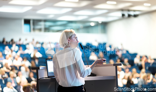 Image of Female speaker giving a talk on corporate business conference. Unrecognizable people in audience at conference hall. Business and Entrepreneurship event.