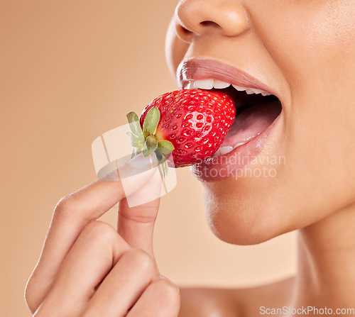 Image of Healthy, eating and a woman taking a bite of a strawberry while isolated on a studio background. Health, organic and a girl tasting a fruit for nutrition, diet or hunger for a snack on a backdrop