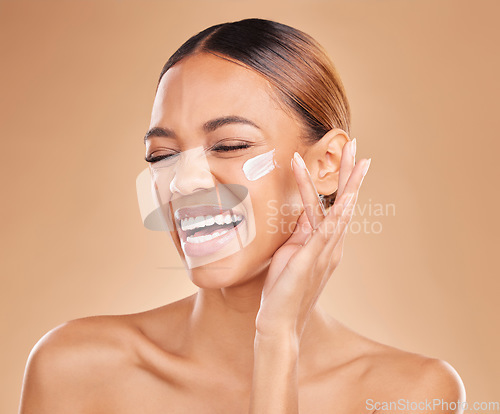 Image of Face skincare, funny and woman with cream in studio isolated on a brown background. Laughing, beauty cosmetics and happy female model apply lotion, creme or facial moisturizer product for skin health