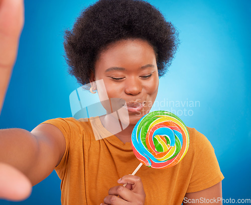 Image of Woman, rainbow lollipop and selfie in studio with a smile and happiness or lgbtq pride on face. Black female model with a color candy on a blue background with sugar, sweets or dessert while excited