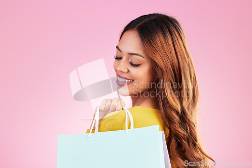 Image of Woman, shopping bag and smile in studio with a customer happy about promotion or discount. Female model or shopper on a pink background for fashion, sale and gift or surprise in mockup paper bags